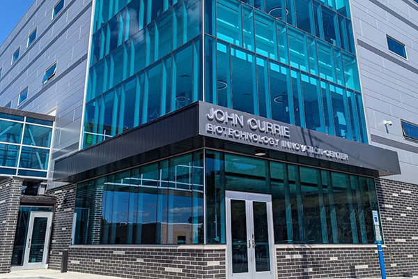 View of building exterior with brick and glass; sign reads John Currie Biotechnology Innovation Center