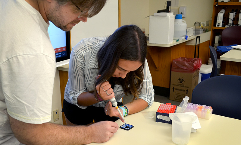 Educator looks on as stund uses pipet to load sample onto DNA chip