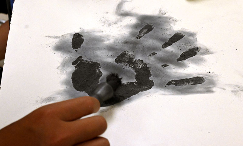 A hand holding a brush used to cover a handprint with black dust