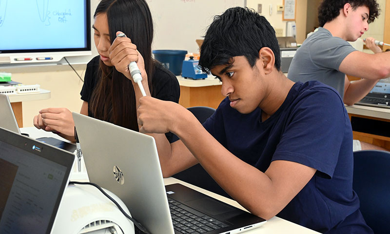 Students at doing lab work with pipettes and laptop computers.