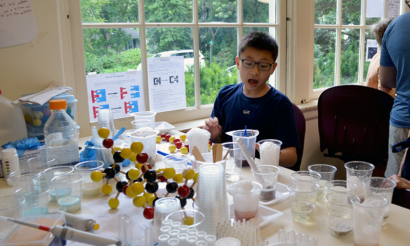 A young student at a desk filled with scientific materials and molecular models.